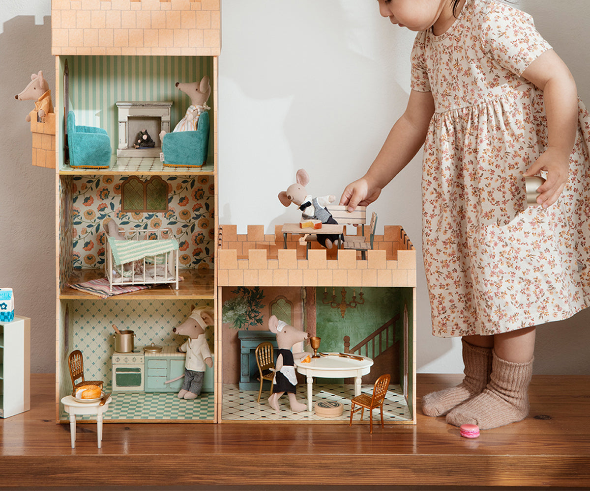 Bambina che gioca accanto a una casa delle bambole Maileg, accessori e topolini in miniatura