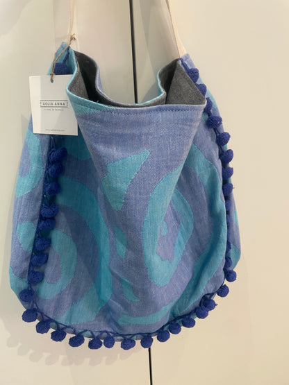 Borsa mare Aelia Anna blu e turchese con pompon decorativi e manici in tessuto, ideale per spiaggia, piscina e vacanze estive.