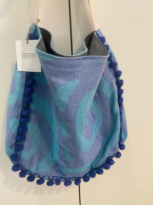 Borsa mare Aelia Anna blu e turchese con pompon decorativi e manici in tessuto, ideale per spiaggia, piscina e vacanze estive.