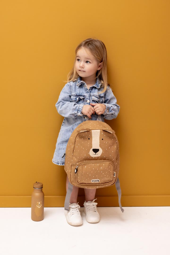 Bambina che tiene in mano lo zainetto Trixie Mr. Orso davanti a sfondo giallo